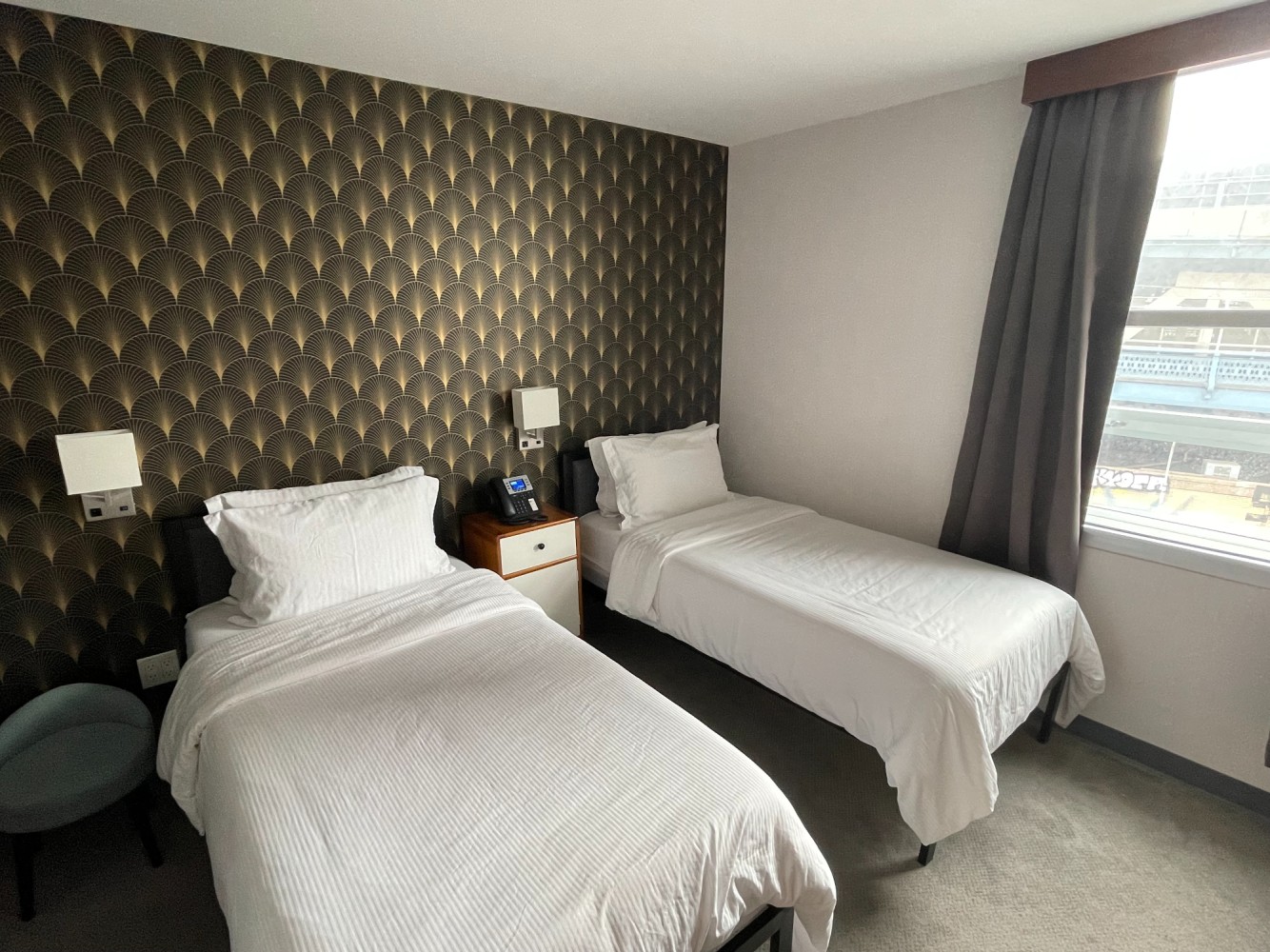 A hotel room with two twin beds, a nightstand, and a window.