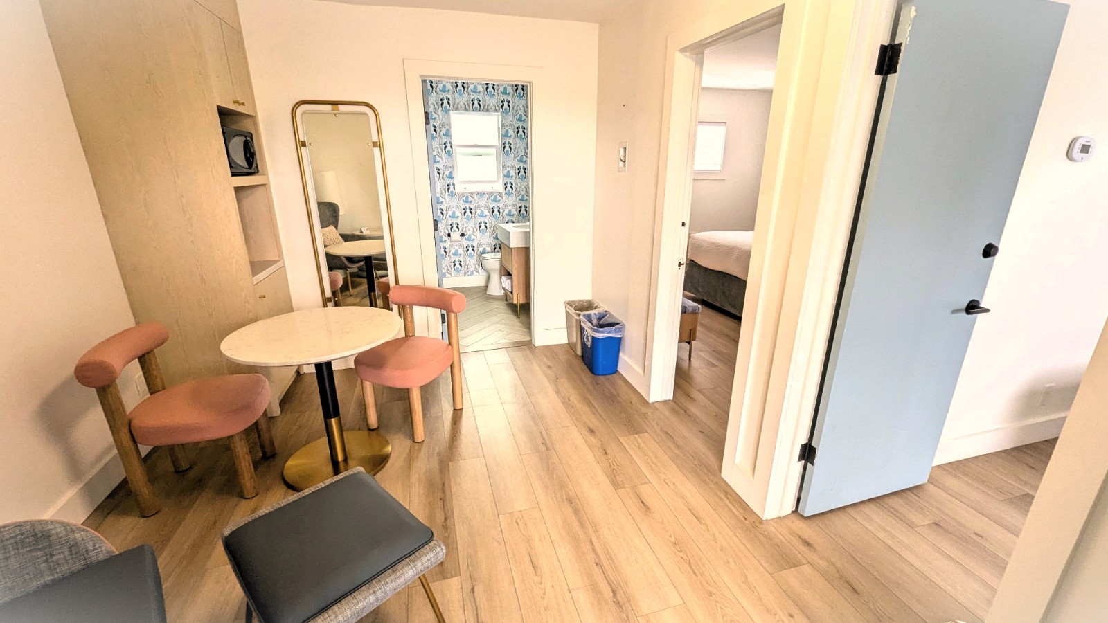A wide view of a hotel room with a table, chairs, and a doorway leading to a bedroom