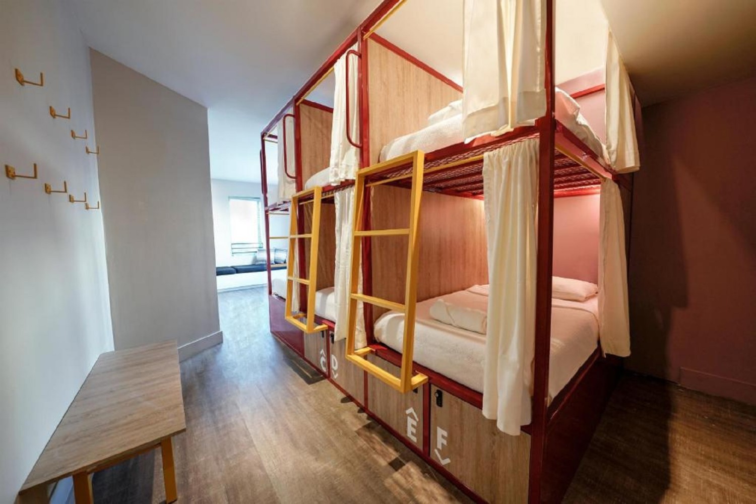 A room with red metal bunk beds, white bedding, and yellow ladders.