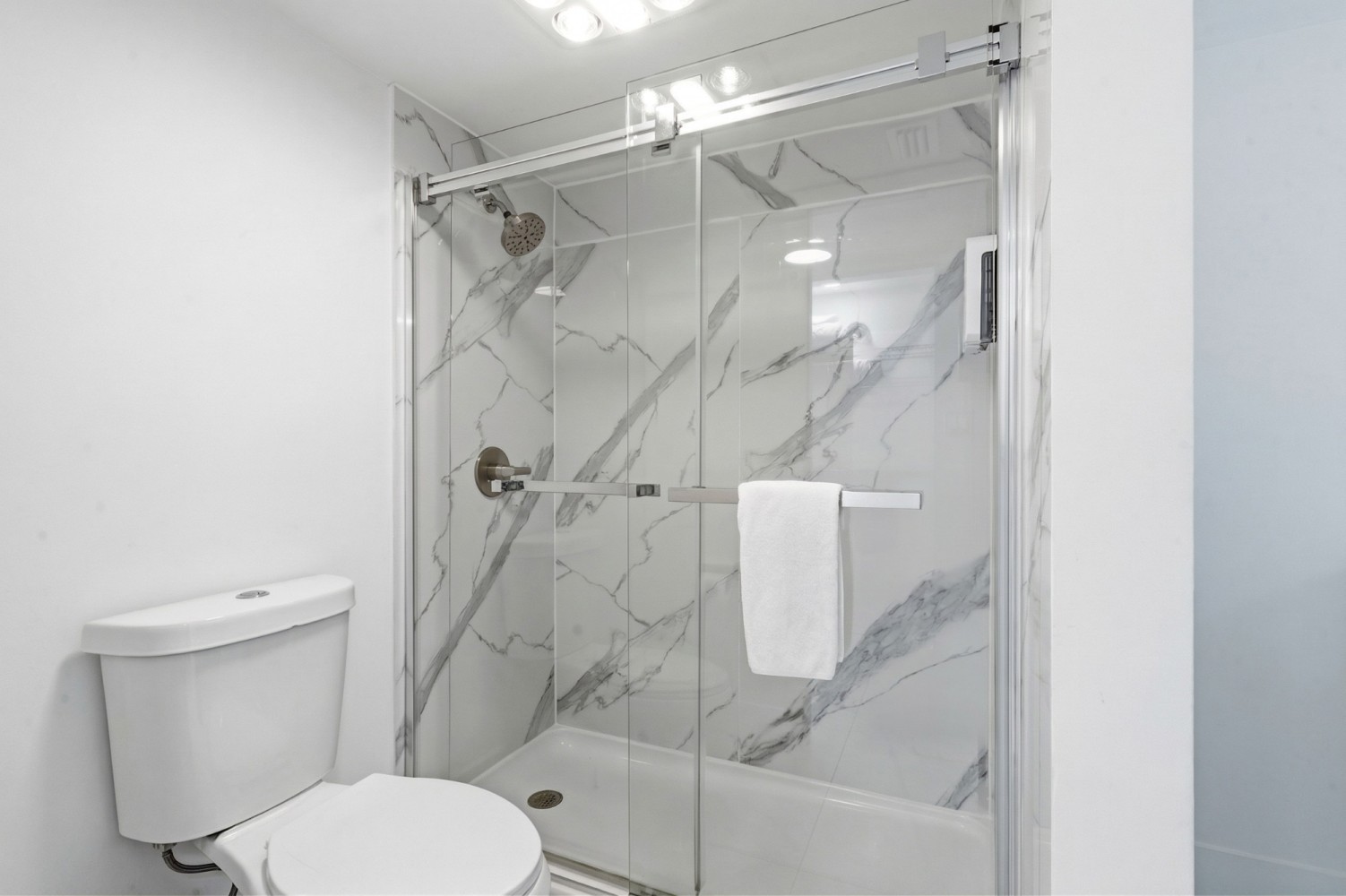 A modern bathroom with a marble-effect shower, toilet, and glass shower door.