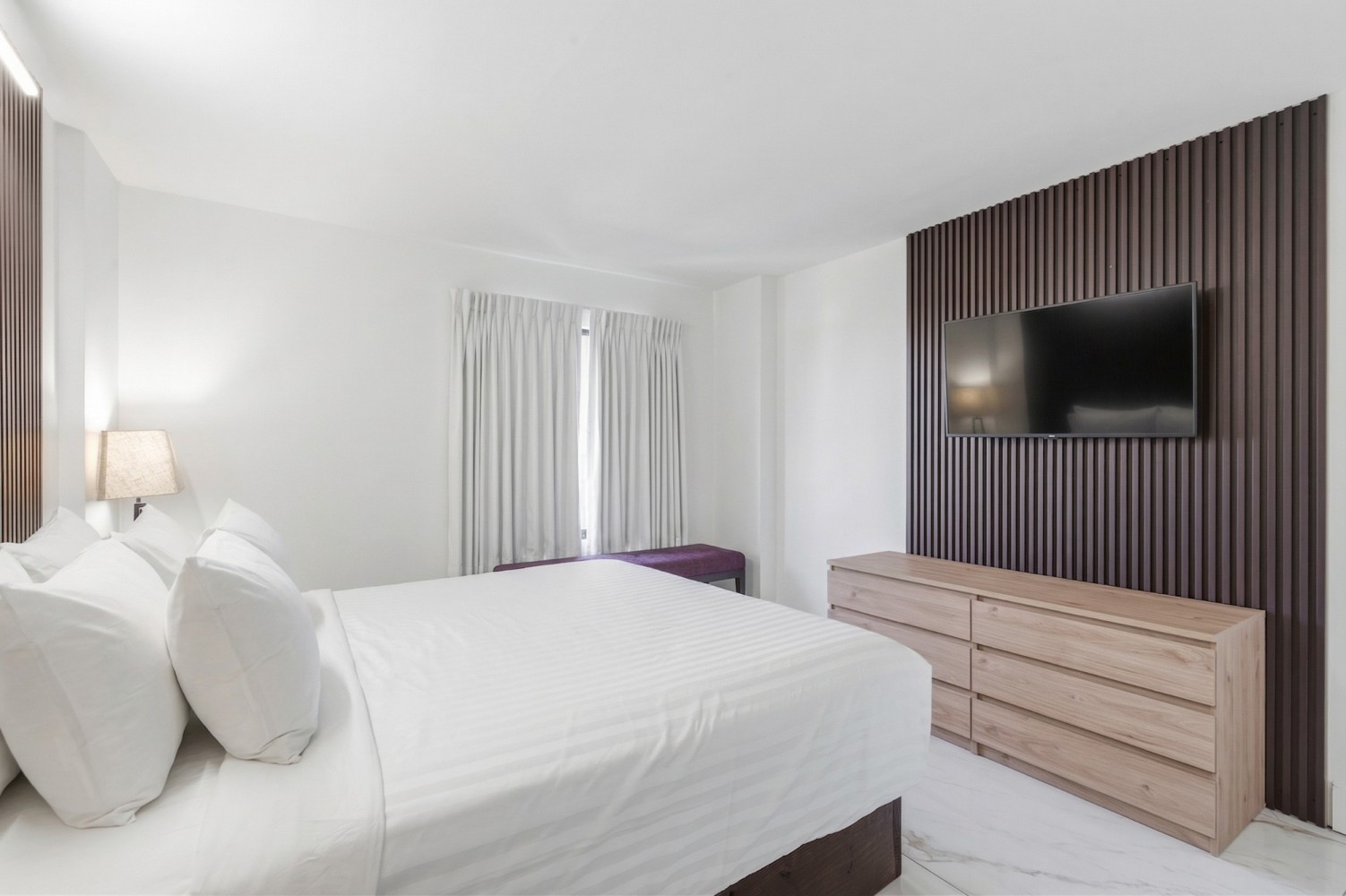 A hotel room with a large bed, dresser, and TV on the wall.