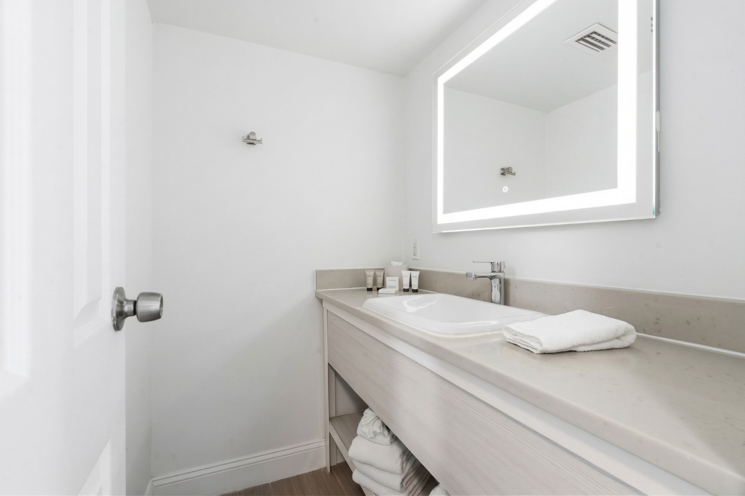 A clean bathroom sink area with a lighted mirror, white sink, and folded towels.