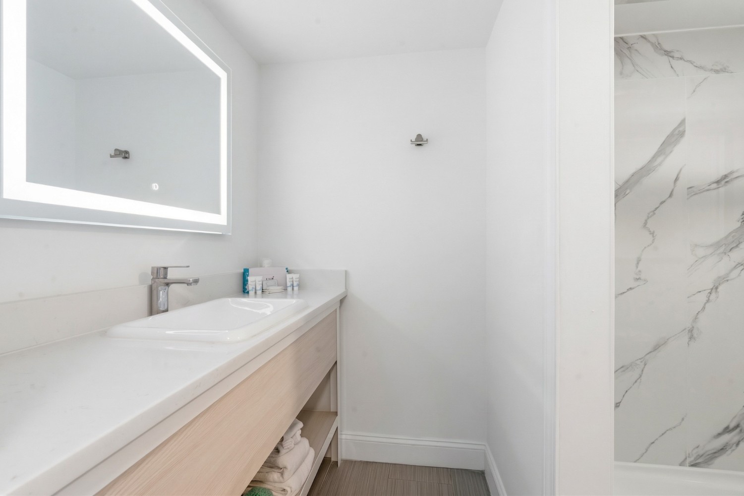 A modern bathroom with a large mirror, a white sink, and a shower with marble walls.