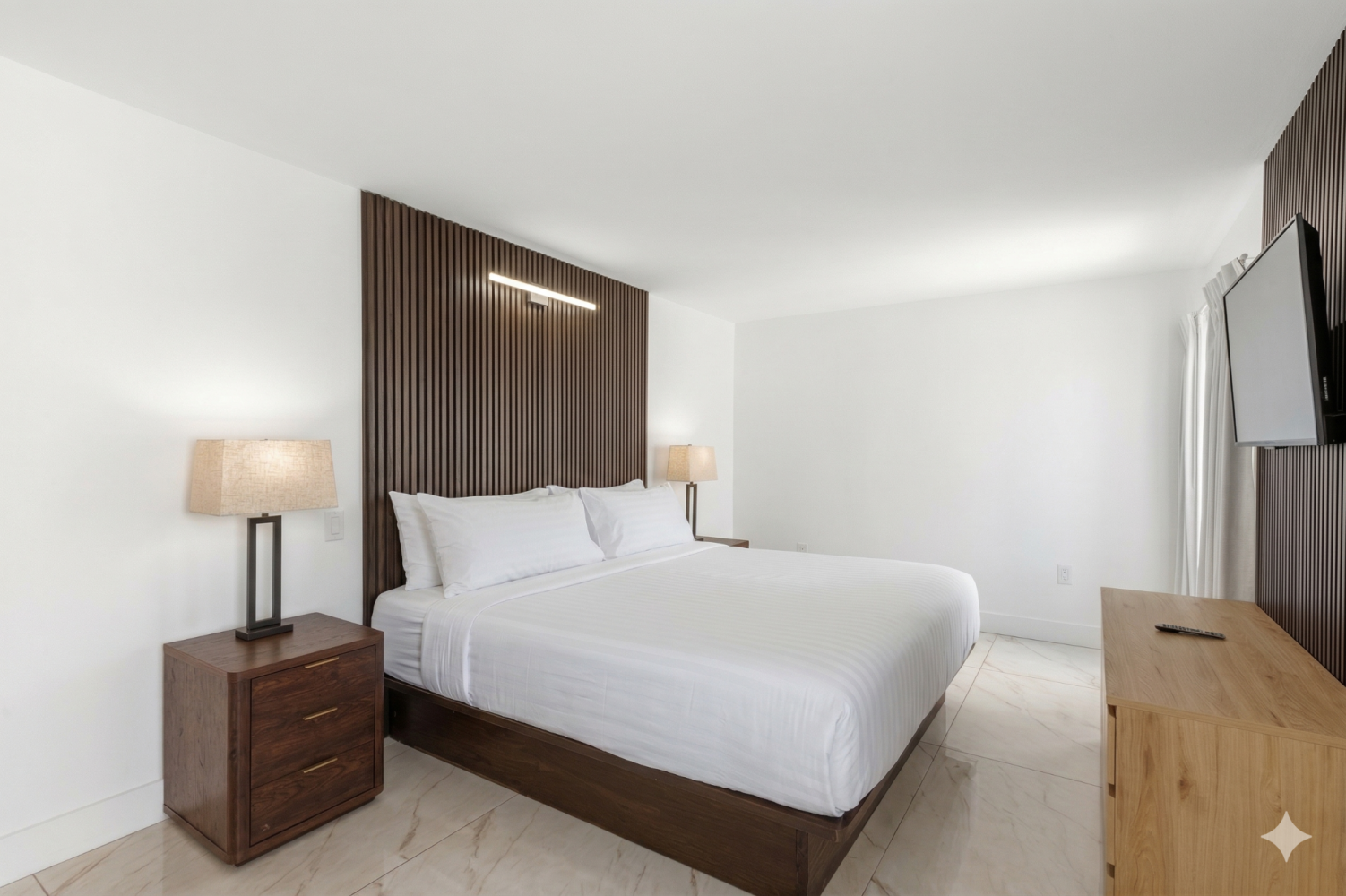 A hotel room with a large bed, two nightstands with lamps, a TV on the wall, and a dresser.