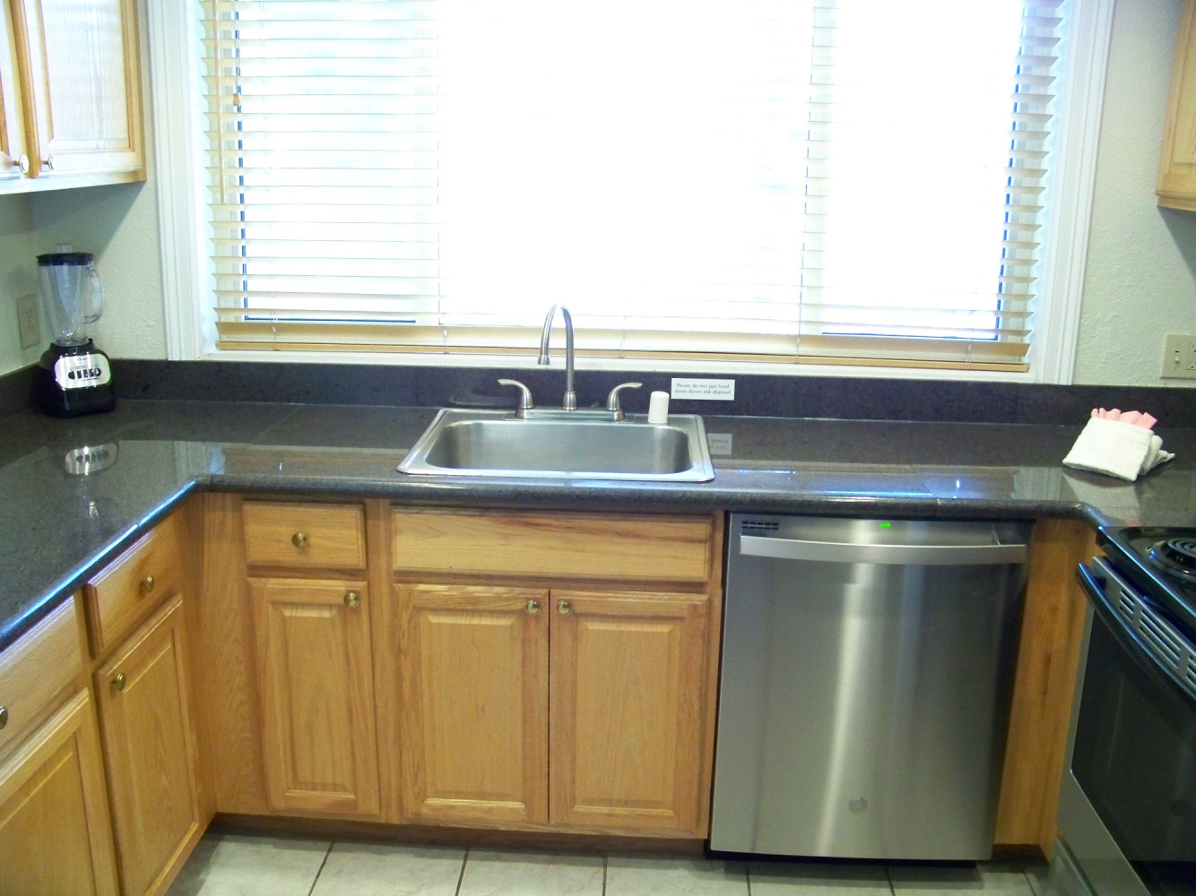 A kitchen with a stainless steel sink, dishwasher, and blender on the countertop.