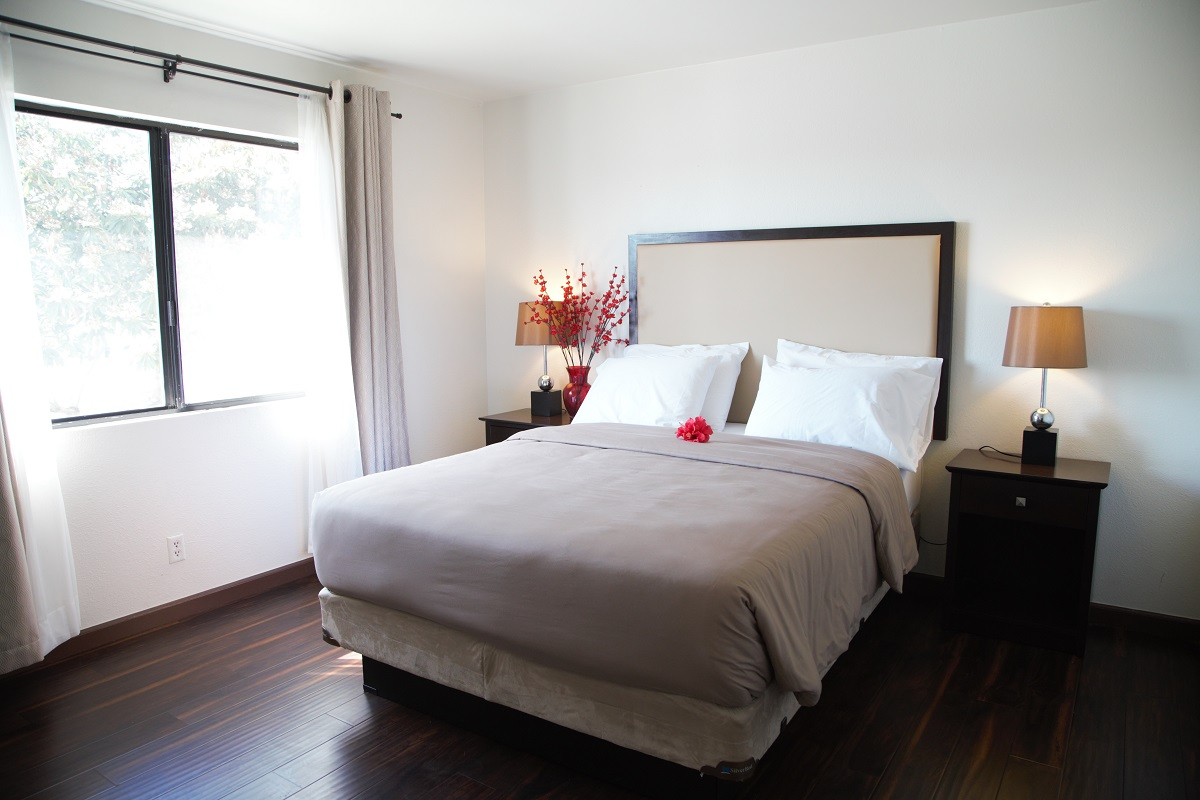 A neatly made hotel room with a bed, two nightstands, and a window.