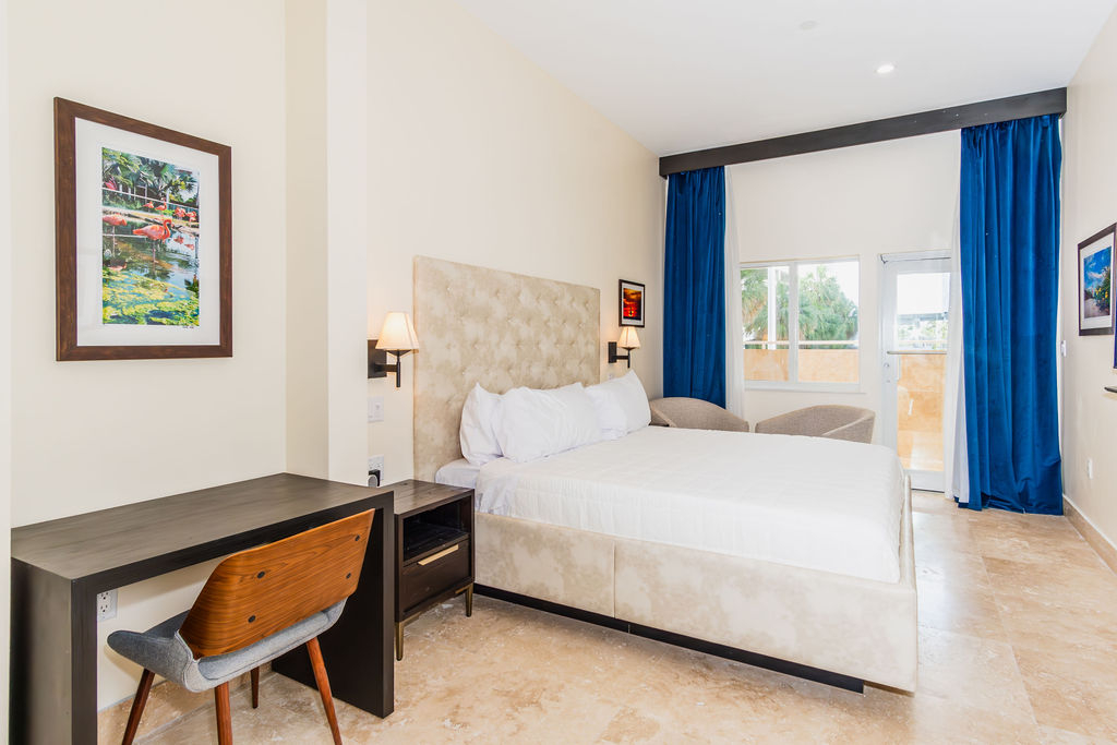 A hotel room with a bed, desk, chair, and artwork on the wall.