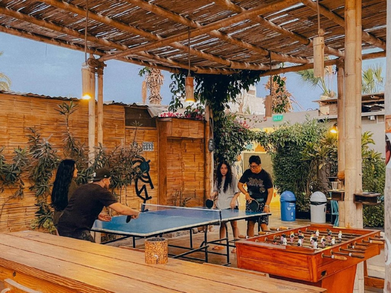 A group of people playing table tennis and foosball in an outdoor recreational area with a pergola.
