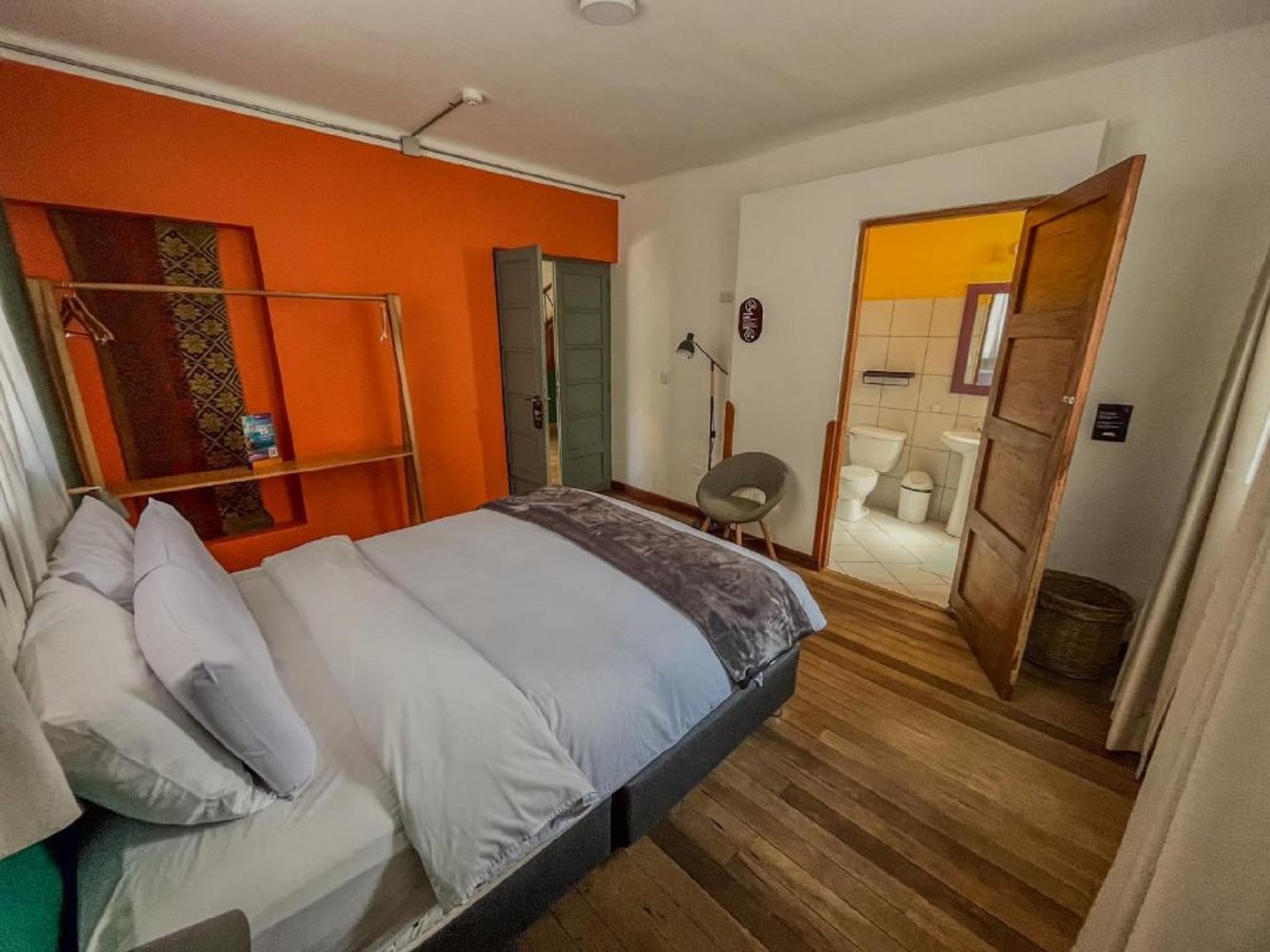 A hotel room with a bed, wooden floor, and open bathroom door
