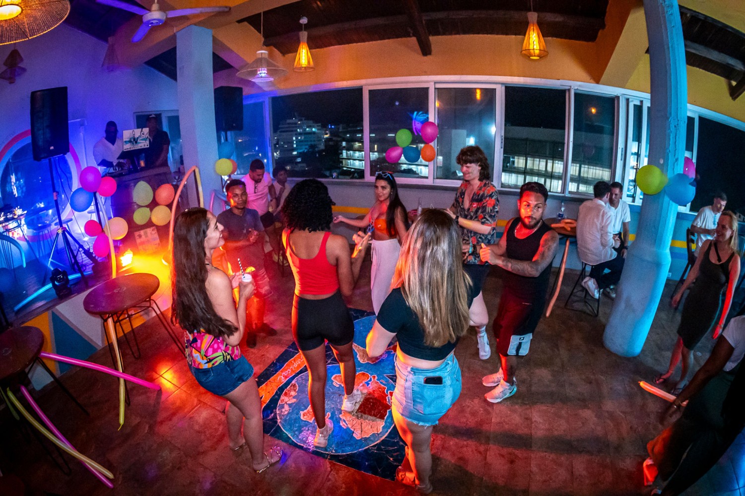 a group of people dancing in a bar with colorful lights and balloons